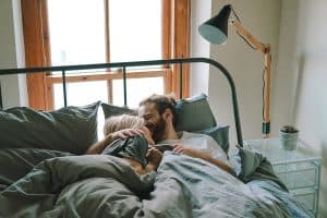 Man is kissing his girlfriend on the forehead (in bed)